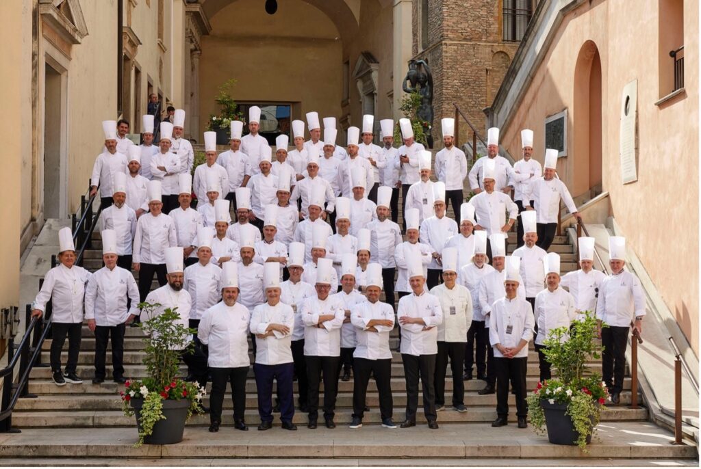 Un grand groupe de chefs vêtus d'uniformes blancs et de toques traditionnelles se sont rassemblés sur les marches d'un bâtiment historique